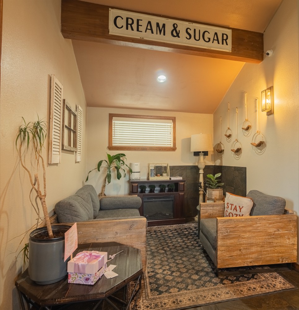 The lounge nook under the Cream and Sugar sign, with wood-framed chairs and warm lamp light