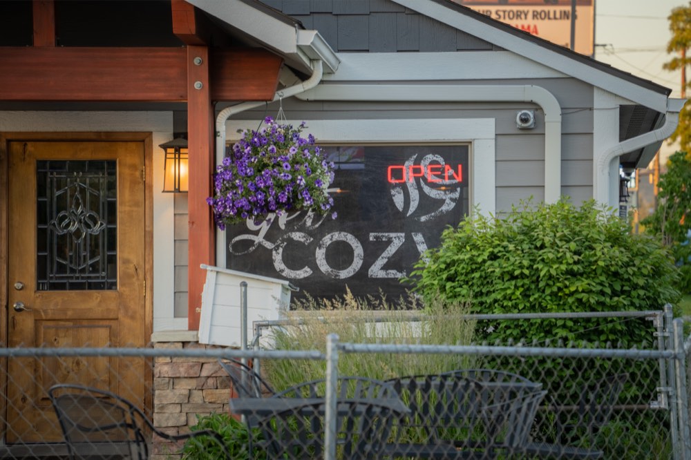 The get COZY chalkboard window with the red neon open sign and hanging flower basket
